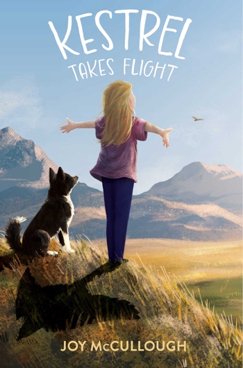 Girl standing on a hill with arms held out. She's facing fields and mountains. Her shadow looks like a bird. A dog stands next to her.